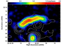 The relic at the outskirts of the galaxy cluster CIZA J2242+53, named „Sausage“ because of its shape, is located at a distance of about two billion light years from us. The contour lines show the intensity of the radio emission at a wavelength of 3 cm, observed with the 100-m Effelsberg radio telescope. The colors represent the distribution of linearly polarized radio intensity at the chosen wavelength, in units of Milli-Jansky per telescope beam. The short dashes indicate the orientation of the magnetic field. The bright source at the bottom is a radio galaxy that belongs to the same galaxy cluster.