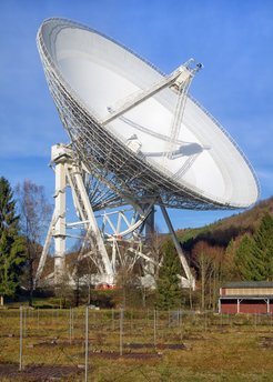 The 100 m Effelsberg Radio Telescope with dipoles of the International LOFAR Telescope in the foreground. The (red-coloured) engines of the elevation drive can be seen at the elevation platform 20 metres above ground. At the Open Day the elevation platform is accessible for small groups of interested visitors. The photo shown here is available in A1 poster size within the new edition of the Effelsberg brochure (“Faltblatt”).