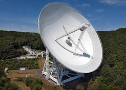 Das 100-m-Radioteleskop Effelsberg mit dahinter liegendem Gebäude des Radioobservatoriums. Hinter der großen Frontscheibe befindet sich der Steuerraum.