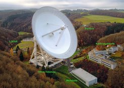 Abb. 2: Das Radio-Observatorium Effelsberg mit dem 100-m-Radioteleskop und der Effelsbergstation des europäischen Niederfrequenz-Radiotelekops LOFAR. Im Vordergrund ist die neue Werkhalle zu sehen, rechts neben dem 100-m-Teleskop das Kontrollgebäude mit Steuerraum und im Hintergrund der Besucherpavillon. Rechts oben am Horizont sieht man den Kirchturm von Lethert.